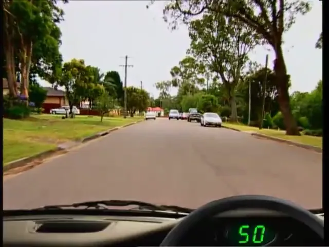 Dashcam view of a suburban two-way street in a 50 km/h zone with parked cars, from a free hazard perception practice clip